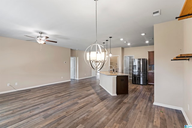 kitchen with light stone counters, pendant lighting, a center island with sink, stainless steel fridge with ice dispenser, and dark hardwood / wood-style flooring