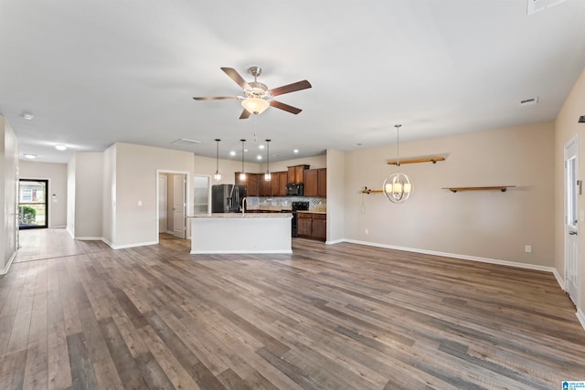 unfurnished living room with ceiling fan with notable chandelier and dark wood-type flooring