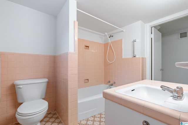 full bathroom featuring tile walls, tiled shower / bath combo, vanity, and toilet