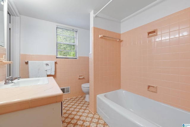 full bathroom with tiled shower / bath, vanity, tile walls, and toilet