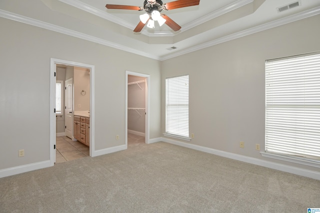 unfurnished bedroom featuring a spacious closet, ceiling fan, ensuite bathroom, ornamental molding, and light colored carpet