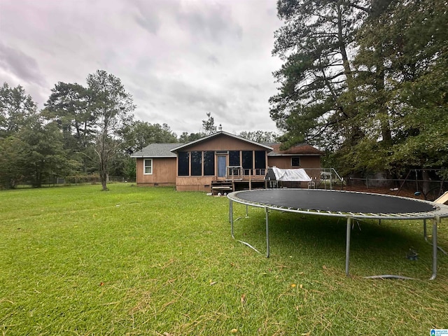 back of property featuring a trampoline, a deck, and a yard