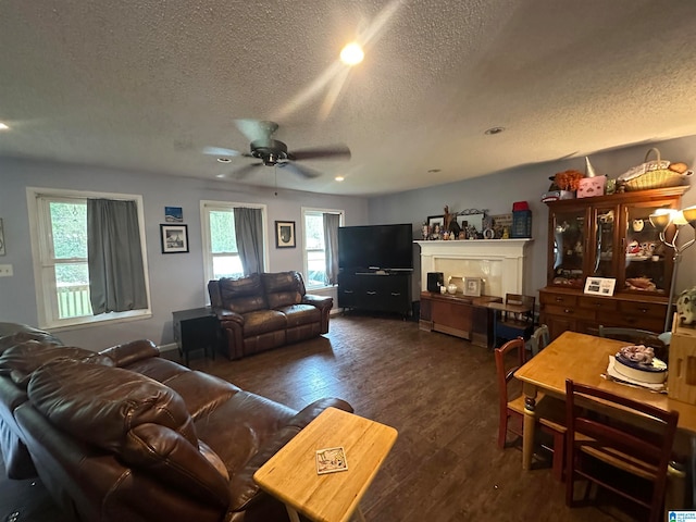 living room with ceiling fan, a fireplace, dark wood-type flooring, and a textured ceiling