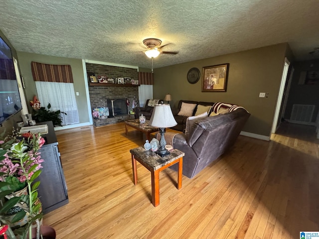 living room with ceiling fan, a textured ceiling, a fireplace, and light wood-type flooring