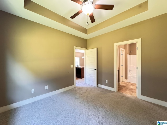 unfurnished bedroom featuring ceiling fan, light colored carpet, and a tray ceiling