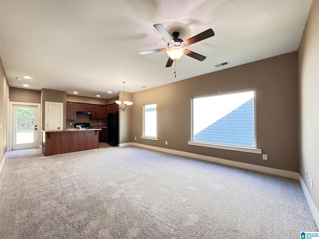 unfurnished living room with light colored carpet, ceiling fan with notable chandelier, and a wealth of natural light