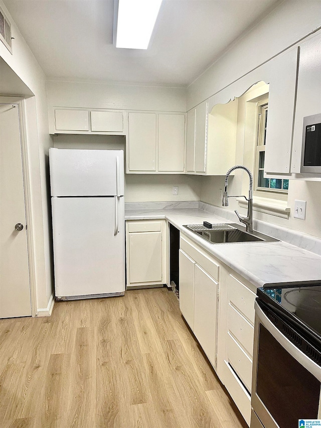 kitchen with appliances with stainless steel finishes, light wood-type flooring, sink, and white cabinetry