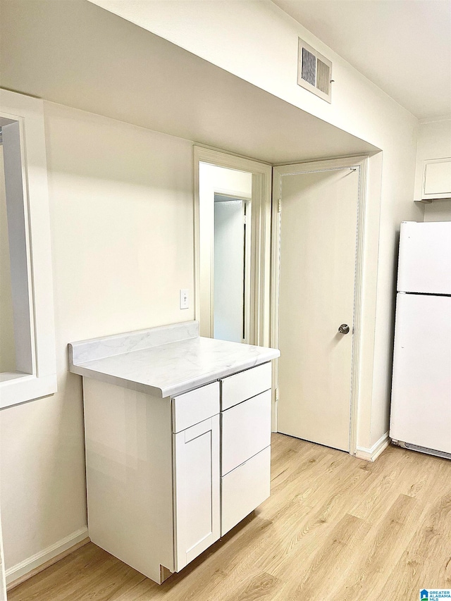 kitchen with light stone counters, white cabinets, white refrigerator, and light wood-type flooring