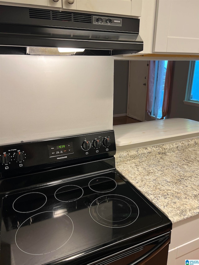 interior details featuring white cabinets, range hood, and black electric range