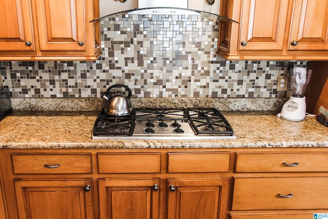 kitchen featuring exhaust hood, light stone countertops, decorative backsplash, and stainless steel gas cooktop