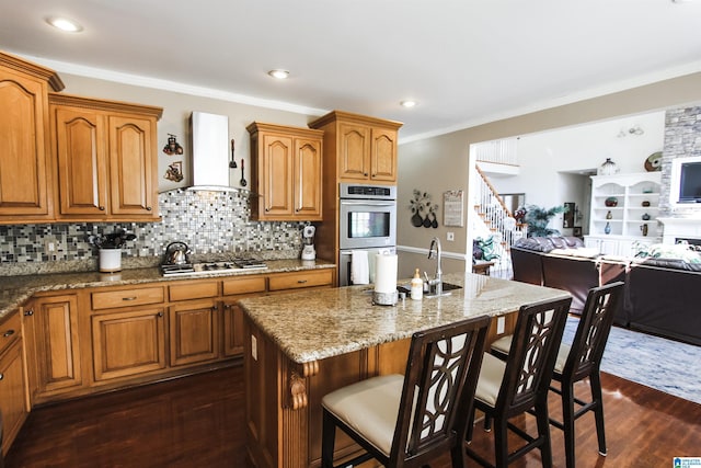 kitchen featuring dark wood finished floors, wall chimney range hood, a breakfast bar, appliances with stainless steel finishes, and open floor plan