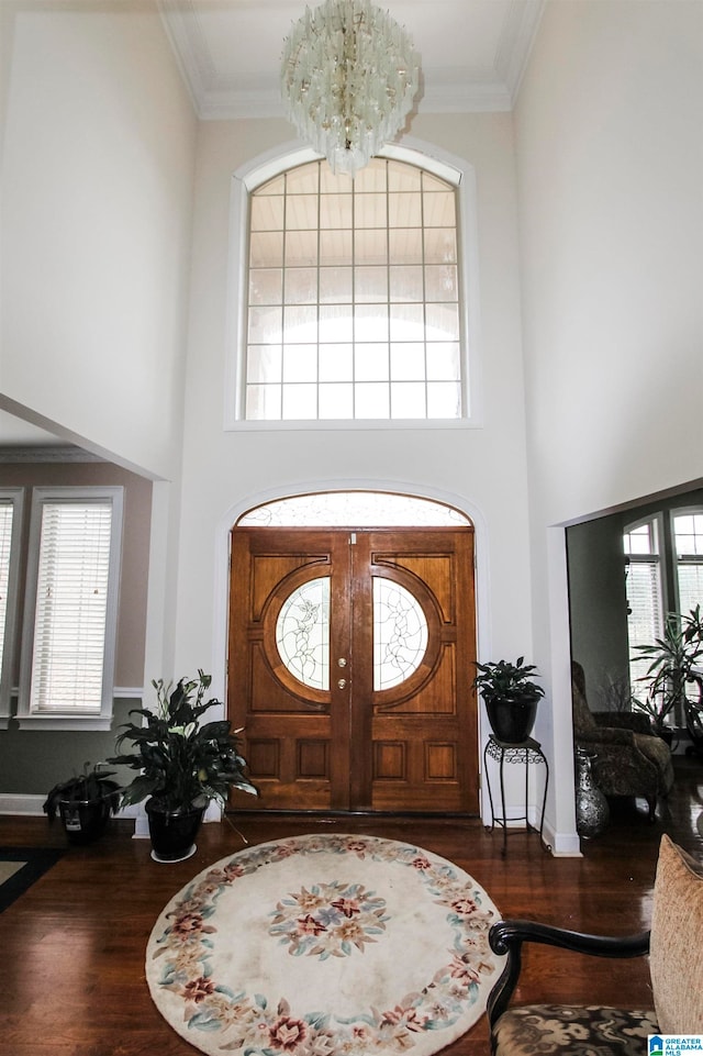 foyer entrance featuring a towering ceiling, a chandelier, dark wood-type flooring, and crown molding