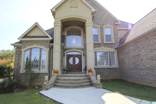 entrance to property featuring roof with shingles, brick siding, and stucco siding