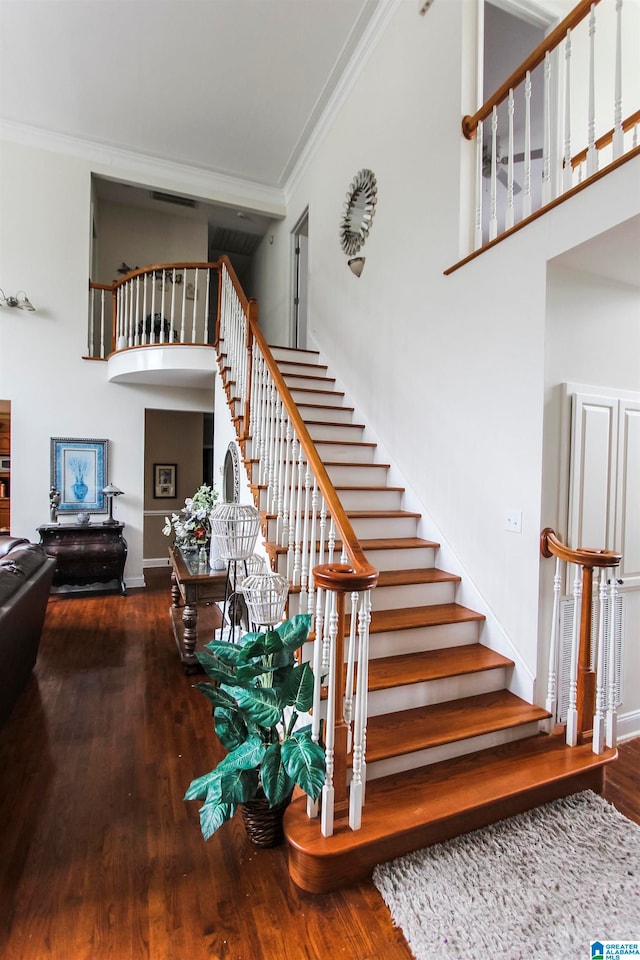 staircase featuring a towering ceiling, crown molding, and hardwood / wood-style floors