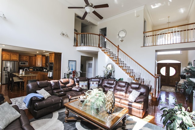 living room featuring a ceiling fan, ornamental molding, stairway, wood finished floors, and a high ceiling