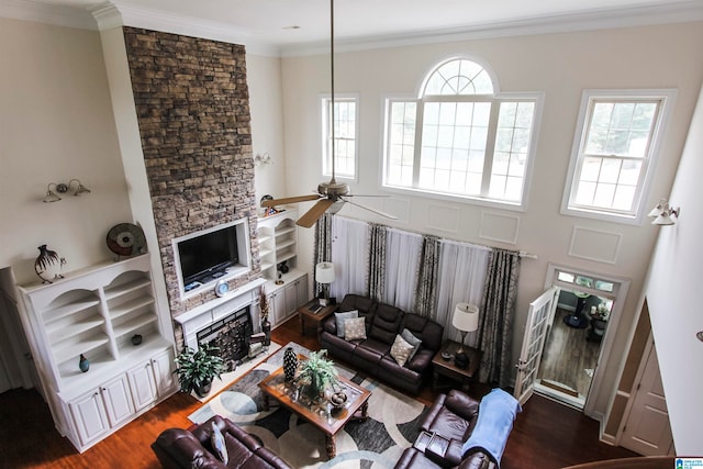 living room featuring ornamental molding, ceiling fan, dark wood-type flooring, and a stone fireplace