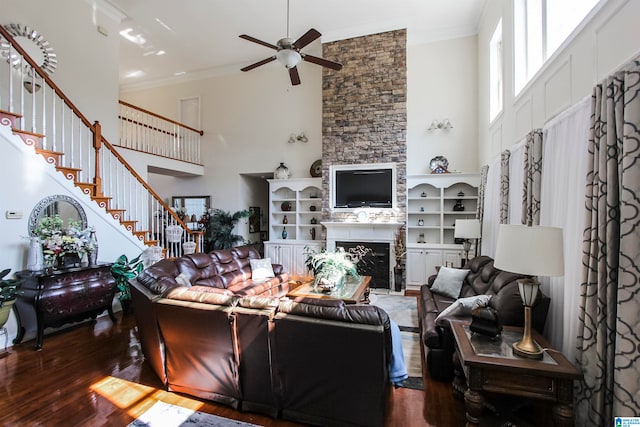 living room with ceiling fan, ornamental molding, a stone fireplace, dark hardwood / wood-style floors, and a high ceiling