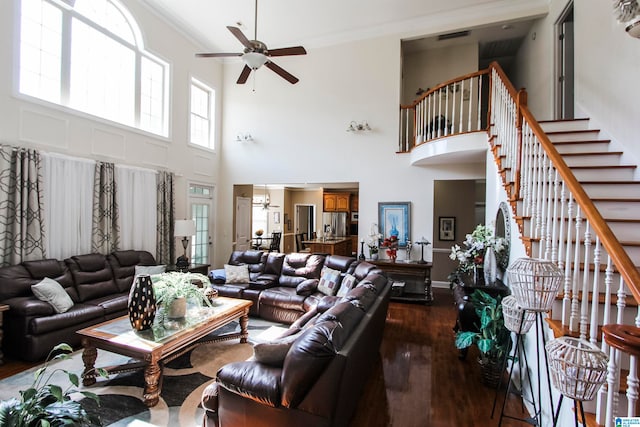 living room with ceiling fan, ornamental molding, a towering ceiling, and dark wood-type flooring