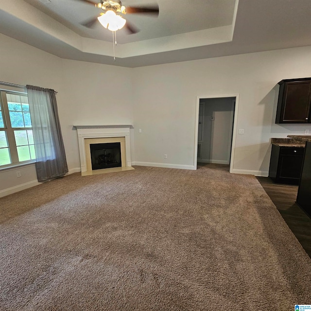 unfurnished living room featuring ceiling fan, a tray ceiling, and dark carpet