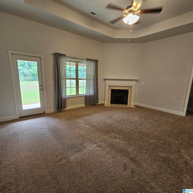 unfurnished living room with ceiling fan, a raised ceiling, carpet, and a healthy amount of sunlight