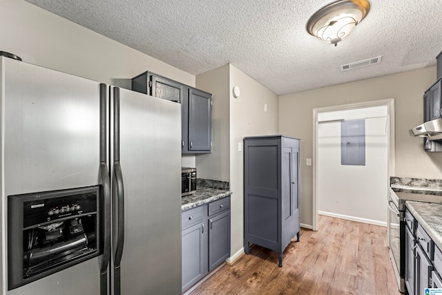 kitchen featuring light wood-type flooring, a textured ceiling, ventilation hood, gray cabinetry, and stainless steel appliances