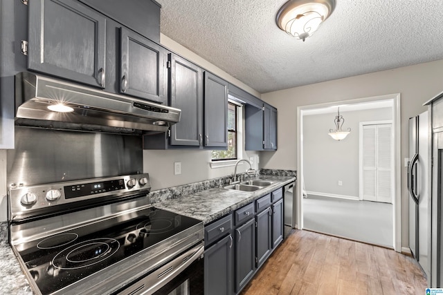 kitchen with light wood-type flooring, a textured ceiling, sink, stainless steel appliances, and decorative light fixtures