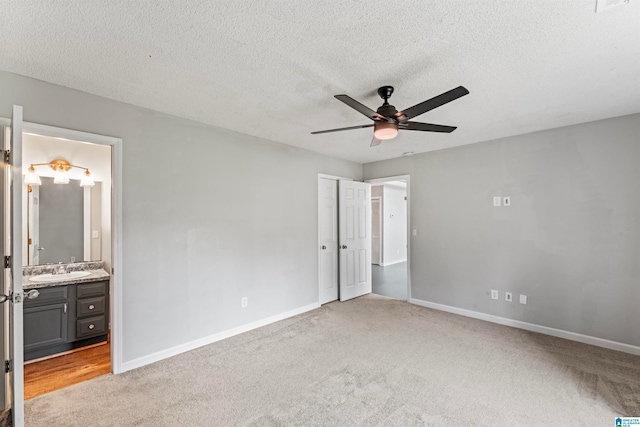 unfurnished bedroom featuring connected bathroom, a textured ceiling, ceiling fan, sink, and light colored carpet