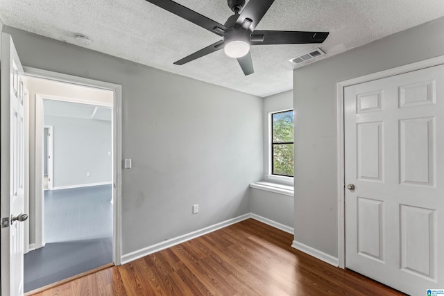 unfurnished bedroom featuring a closet, a textured ceiling, ceiling fan, and dark hardwood / wood-style flooring