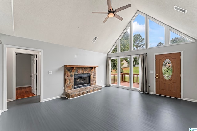 unfurnished living room with a textured ceiling, dark wood-type flooring, high vaulted ceiling, a stone fireplace, and ceiling fan