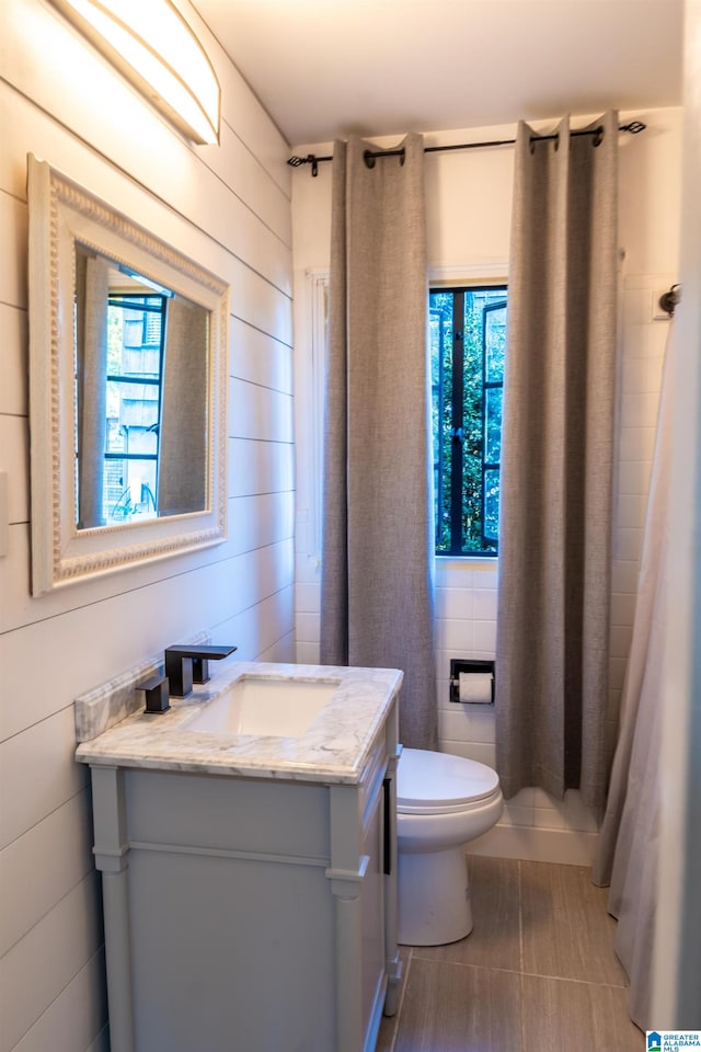 bathroom featuring curtained shower, wooden walls, vanity, and toilet