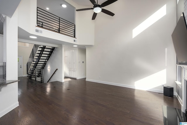 unfurnished living room featuring ceiling fan, dark hardwood / wood-style flooring, and a towering ceiling