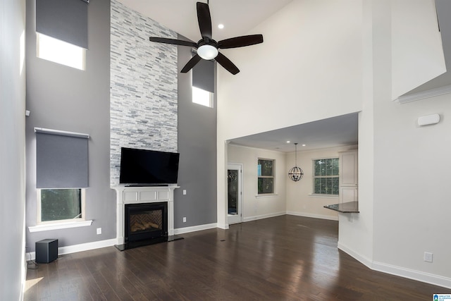 unfurnished living room with ceiling fan, a large fireplace, a towering ceiling, and dark wood-type flooring