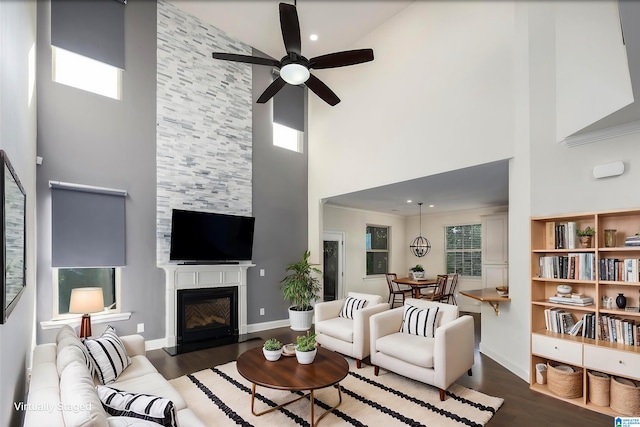 living room featuring a fireplace, ceiling fan, dark wood-type flooring, and a high ceiling