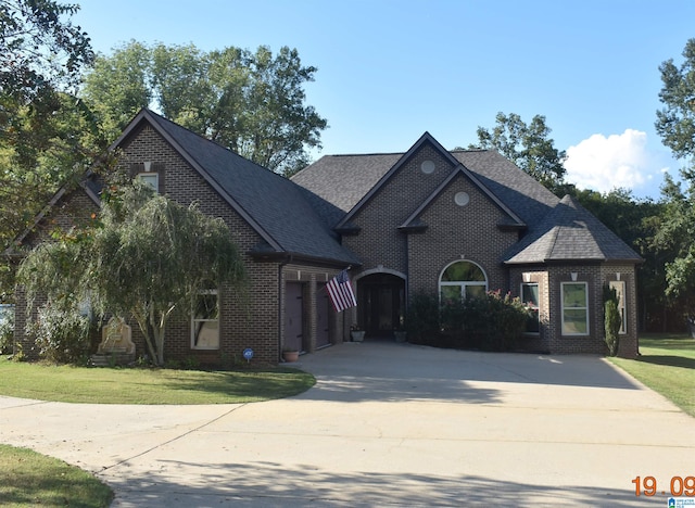 view of front of house with brick siding, driveway, a front yard, and roof with shingles