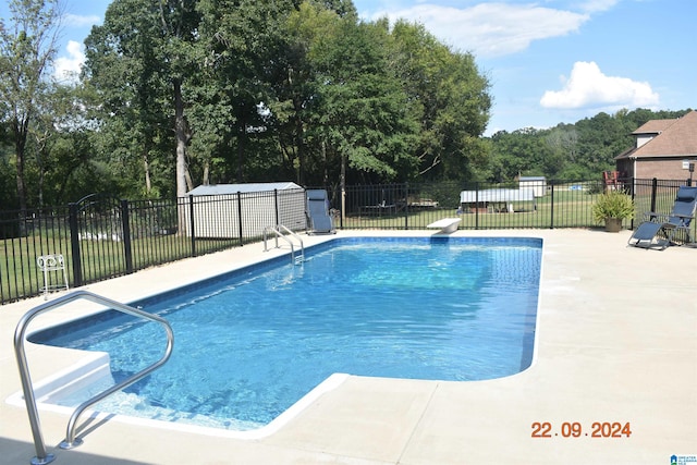 view of swimming pool with an outdoor structure, a diving board, and a patio