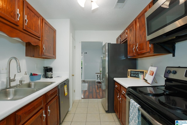 kitchen with appliances with stainless steel finishes, a textured ceiling, light tile patterned flooring, and sink