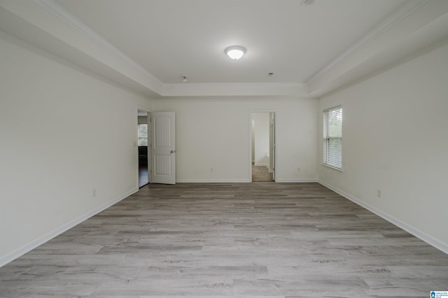 empty room featuring crown molding, a raised ceiling, and light wood-type flooring