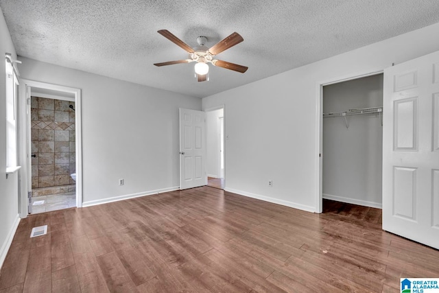 unfurnished bedroom with ensuite bath, a textured ceiling, ceiling fan, wood-type flooring, and a closet