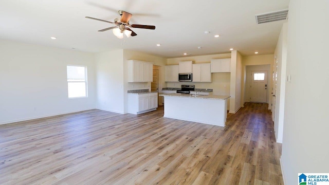 kitchen featuring white cabinetry, light stone counters, a kitchen island with sink, appliances with stainless steel finishes, and light wood-type flooring