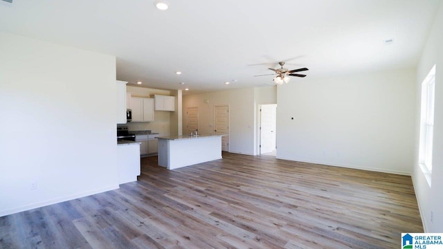 kitchen featuring light wood-type flooring, a kitchen island, ceiling fan, white cabinetry, and stainless steel range with electric cooktop