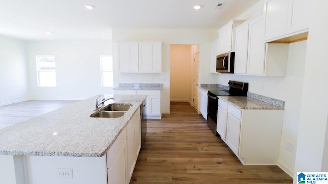 kitchen with electric range, white cabinetry, and an island with sink