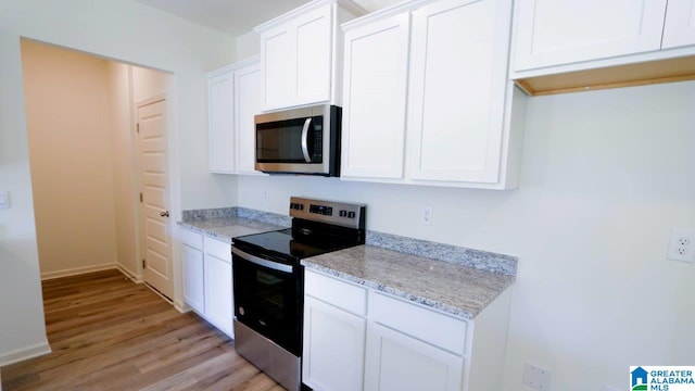 kitchen with light stone countertops, white cabinetry, stainless steel appliances, and light hardwood / wood-style flooring