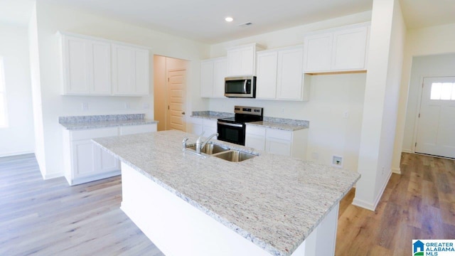 kitchen with a kitchen island with sink, sink, light hardwood / wood-style floors, white cabinetry, and stainless steel appliances