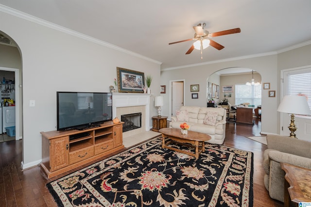 living room featuring ceiling fan with notable chandelier, washer and dryer, ornamental molding, dark hardwood / wood-style flooring, and a tiled fireplace