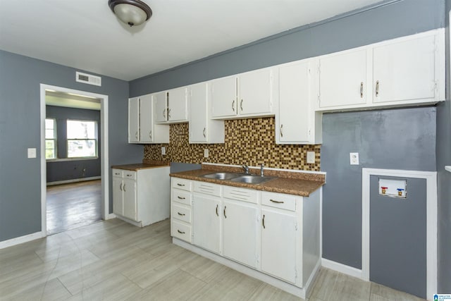7749 5th Ave, Birmingham, AL 35206 - kitchen with a sink, decorative backsplash, dark countertops, white cabinetry, and baseboards