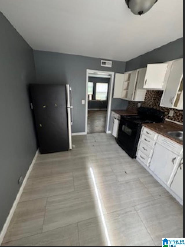 kitchen featuring black range oven, stainless steel fridge, white cabinetry, and tasteful backsplash