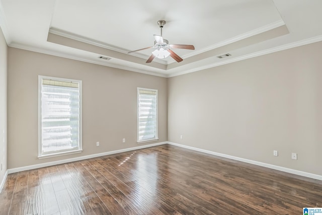 empty room with a raised ceiling, crown molding, dark wood-type flooring, and ceiling fan