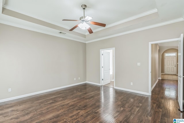 empty room featuring arched walkways, dark wood-style flooring, visible vents, a ceiling fan, and a tray ceiling