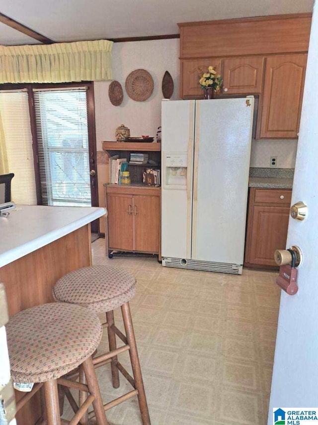 kitchen featuring white fridge with ice dispenser, a kitchen bar, and crown molding