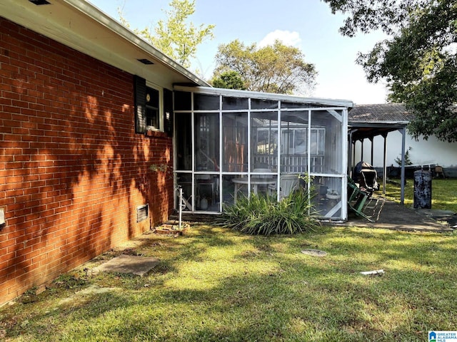view of side of property featuring a sunroom, brick siding, and a lawn